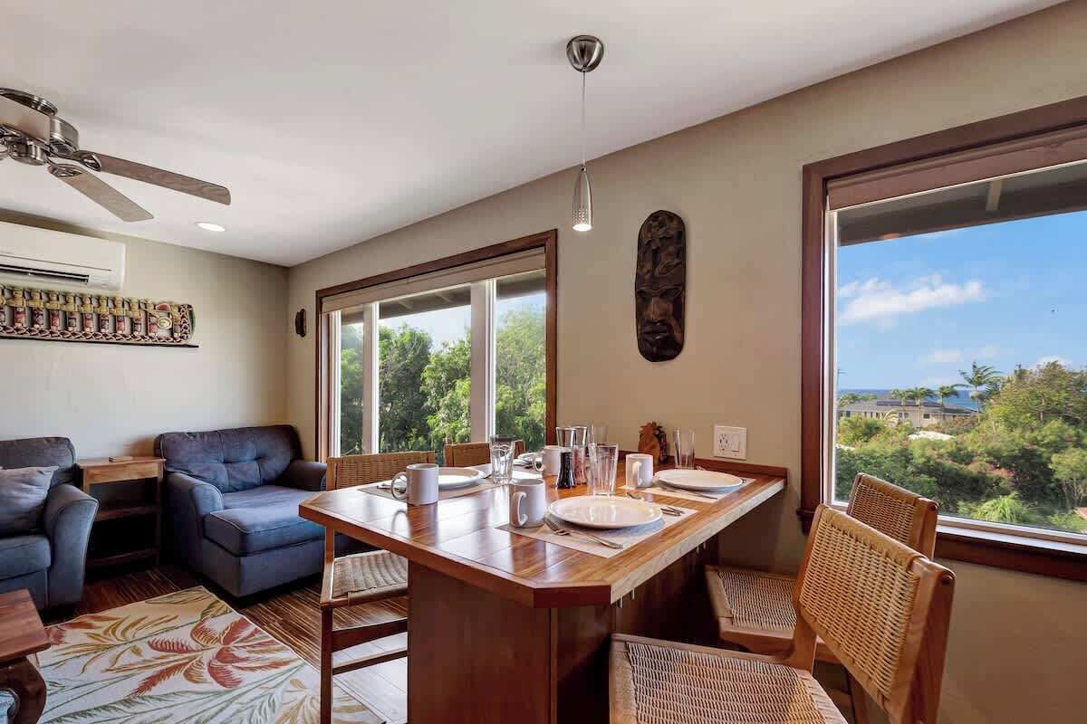 A dining area with a wooden table, chairs, and a view of greenery outside.
