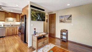 A modern kitchen with wooden cabinets, a stainless steel refrigerator, and a large window displaying a waterfall.