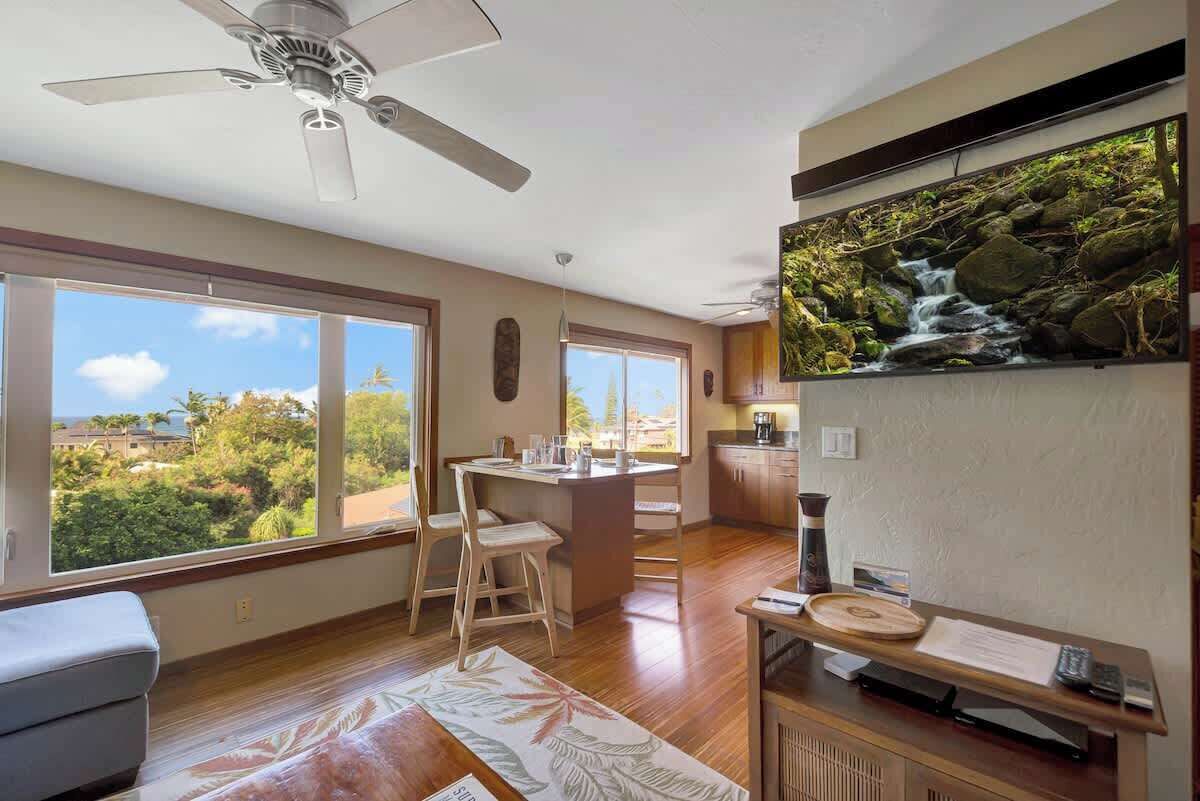 A modern kitchen with a large island, wooden flooring, and a view of a waterfall through a large window.