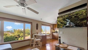 A modern kitchen with a large island, wooden flooring, and a view of a waterfall through a large window.