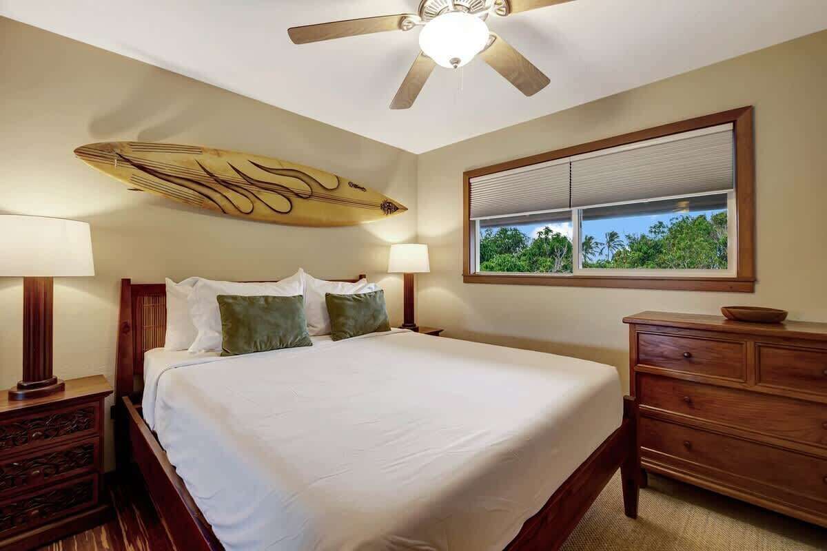A bedroom with a bed, bedside tables, a ceiling fan, a window with a view, and a wooden headboard.