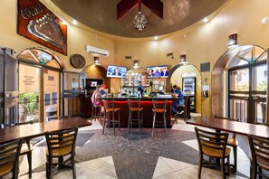 A bar area with a counter, stools, and a television screen. There are tables and chairs around the bar.