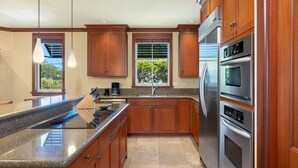A modern kitchen with granite countertops, stainless steel appliances, wooden cabinets, and pendant lighting.