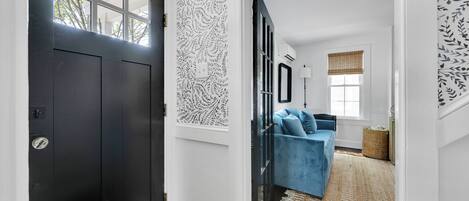 Um corredor com uma porta preta, um sofá azul e um papel de parede estampado.