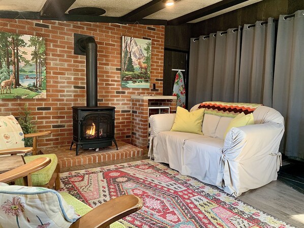 Una sala de estar acogedora con chimenea de ladrillo, un sofá blanco, un tapete estampado y una silla de madera.