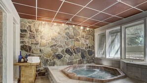 A bathroom with a stone wall, a wooden vanity, a bathtub, and a window with blinds. - Stunning Ski-In Ski-Out Condo/Private Hot Tub/Recently Updated (Dillon)