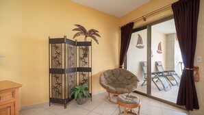 A room with a large sliding glass door leading to a balcony with beach chairs and a view of the sea.