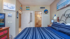 A bedroom with a bed, a nightstand, a TV, and a door leading to a bathroom. - Princesa Resort D-104 Dream Catcher  Comfy Ground Floor Condo (Puerto Penasco)
