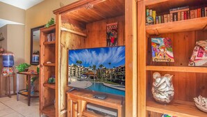 A wooden entertainment center with a flat-screen TV, books, decorative items, and a water dispenser. - Princesa Resort D-104 Dream Catcher  Comfy Ground Floor Condo (Puerto Penasco)