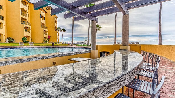 A pool area with a marble bar and outdoor seating, overlooking a body of water. - Princesa Resort D-104 Dream Catcher  Comfy Ground Floor Condo (Puerto Penasco)