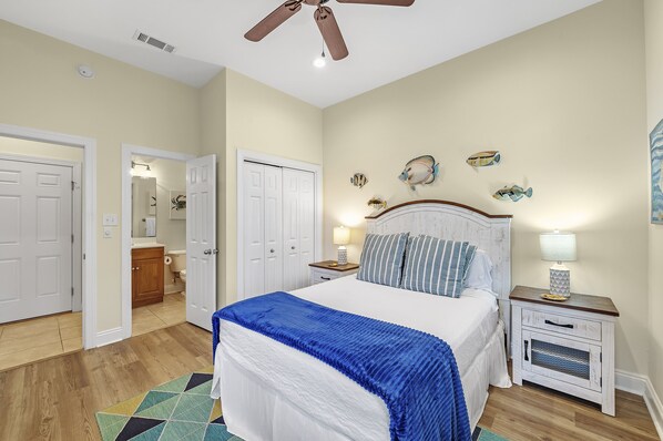 Un dormitorio con cama, mesitas de noche, ventilador de techo y decoración de peces en la pared.