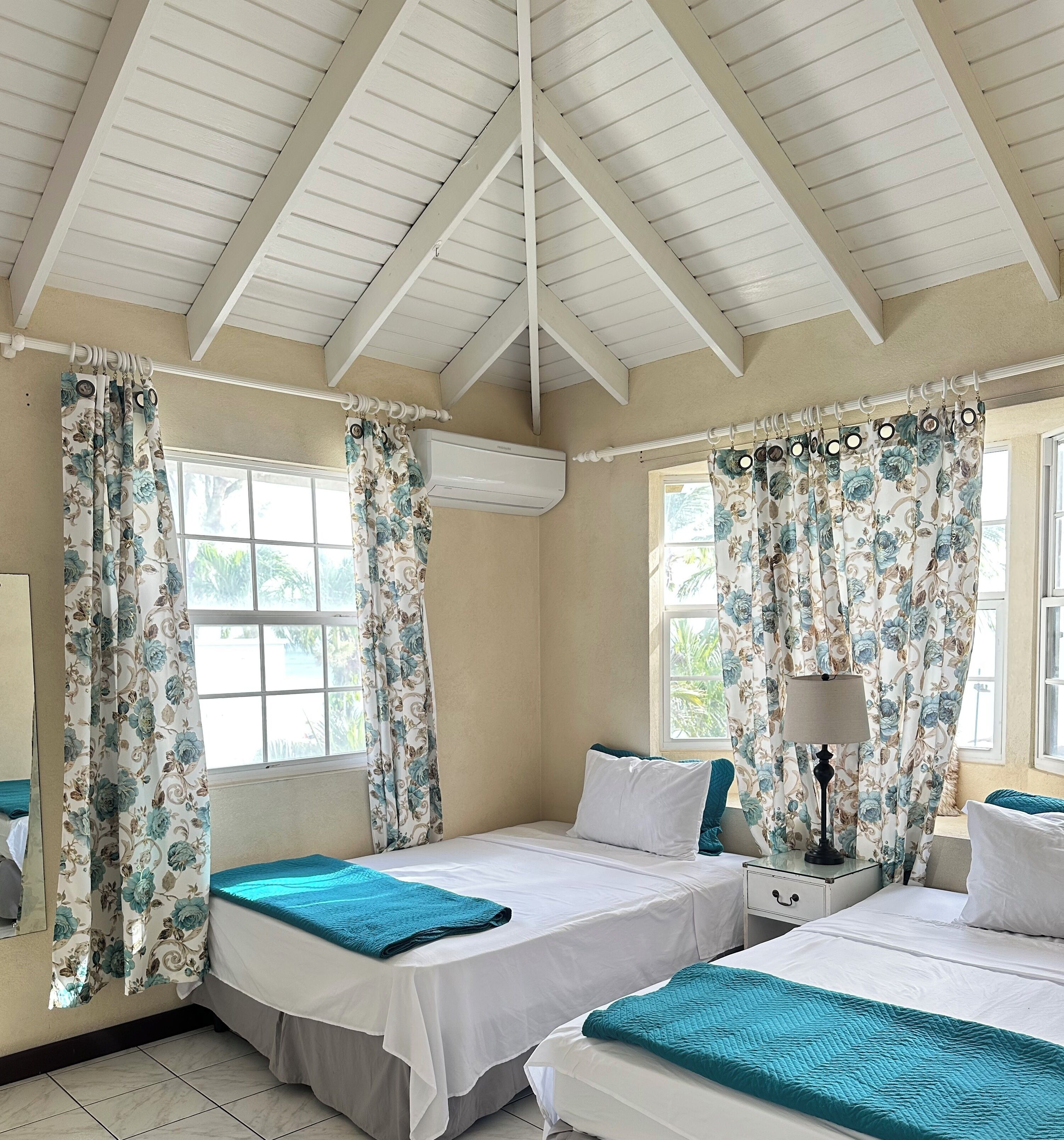 A room with two beds, a window, an air conditioning unit, and a lamp.