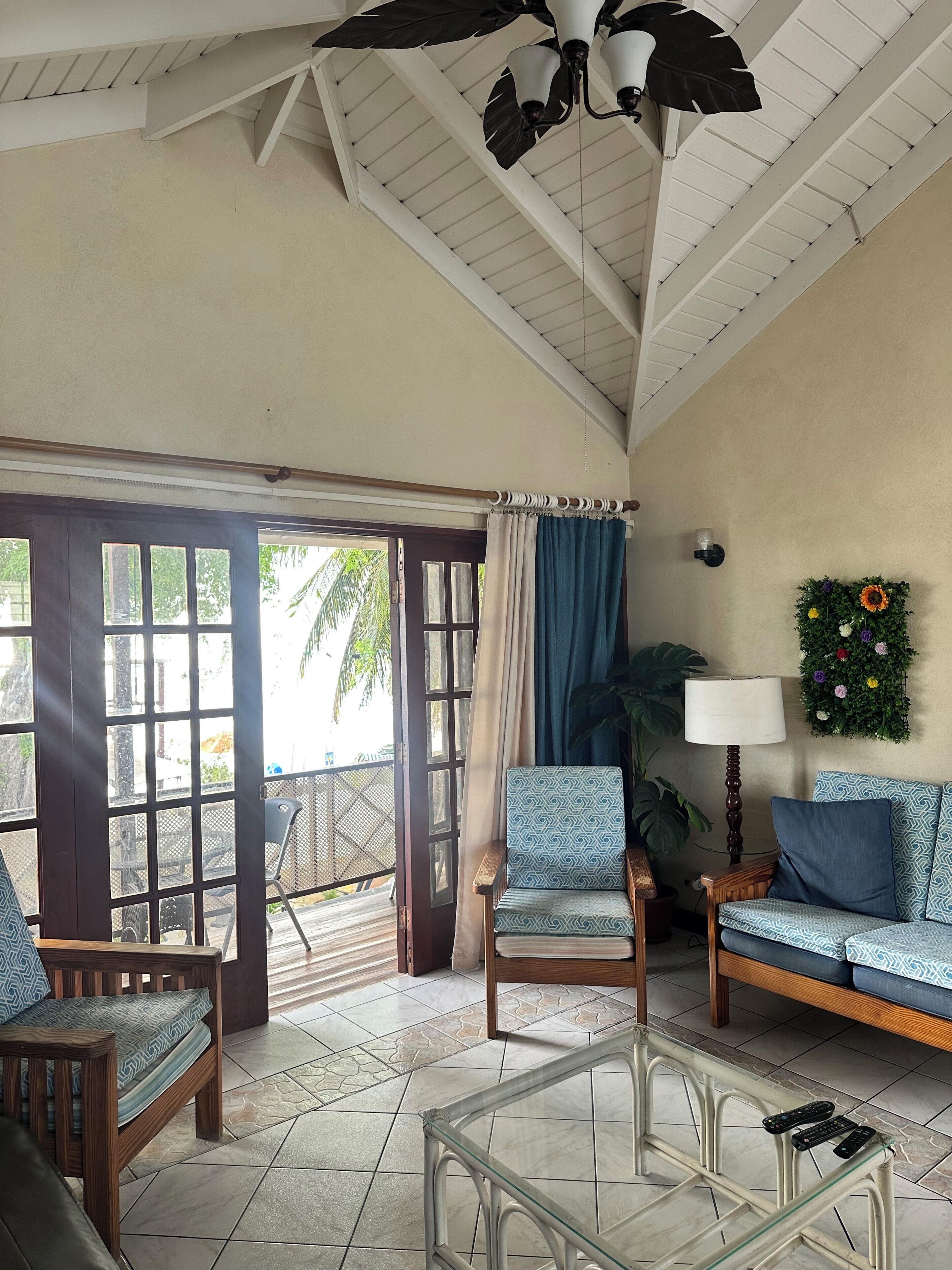 A room with a ceiling fan, a sofa, a chair, a glass coffee table, and a view through a door to an outdoor area.
