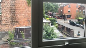 A window view of a street with brick buildings, a café, and a parked car.