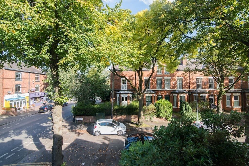 Een woonstraat met bakstenen huizen, geparkeerde auto's en bomen.