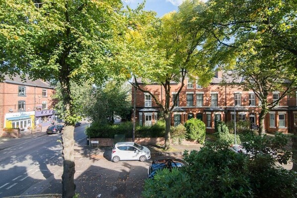 A residential street with brick houses, parked cars, and trees.