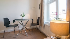 A room with a glass table, two chairs, a lamp, and a window with curtains.