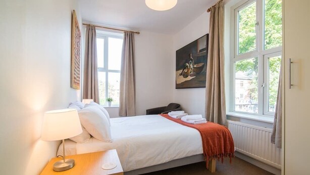 A hotel room with a bed, bedside table, lamp, and a painting on the wall.
