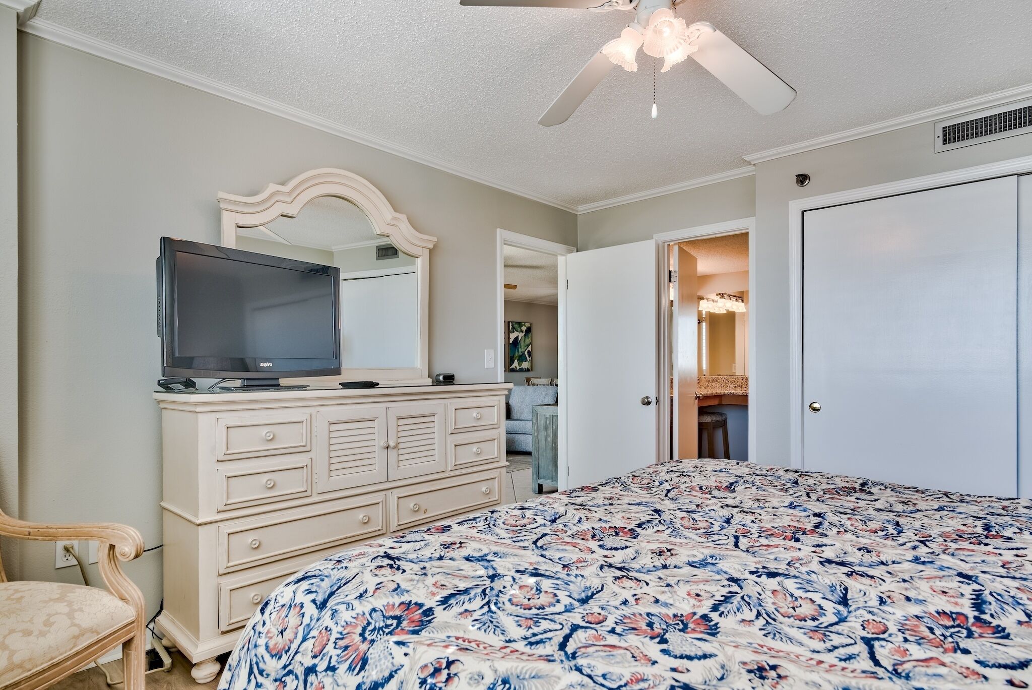 A bedroom with a bed, dresser, television, and ceiling fan.
