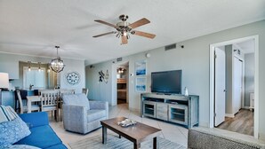 Amplia sala de estar con ventilador de techo, televisor y comedor con mesa y sillas.