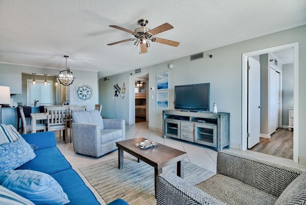 A spacious living room with a ceiling fan, a television, and a dining area with a table and chairs. - Sunset Views & Fireworks Nights – Islander 616 (Destin)