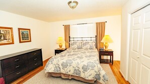 Een slaapkamer met een bed, nachtkastjes, een dressoir en een deur.