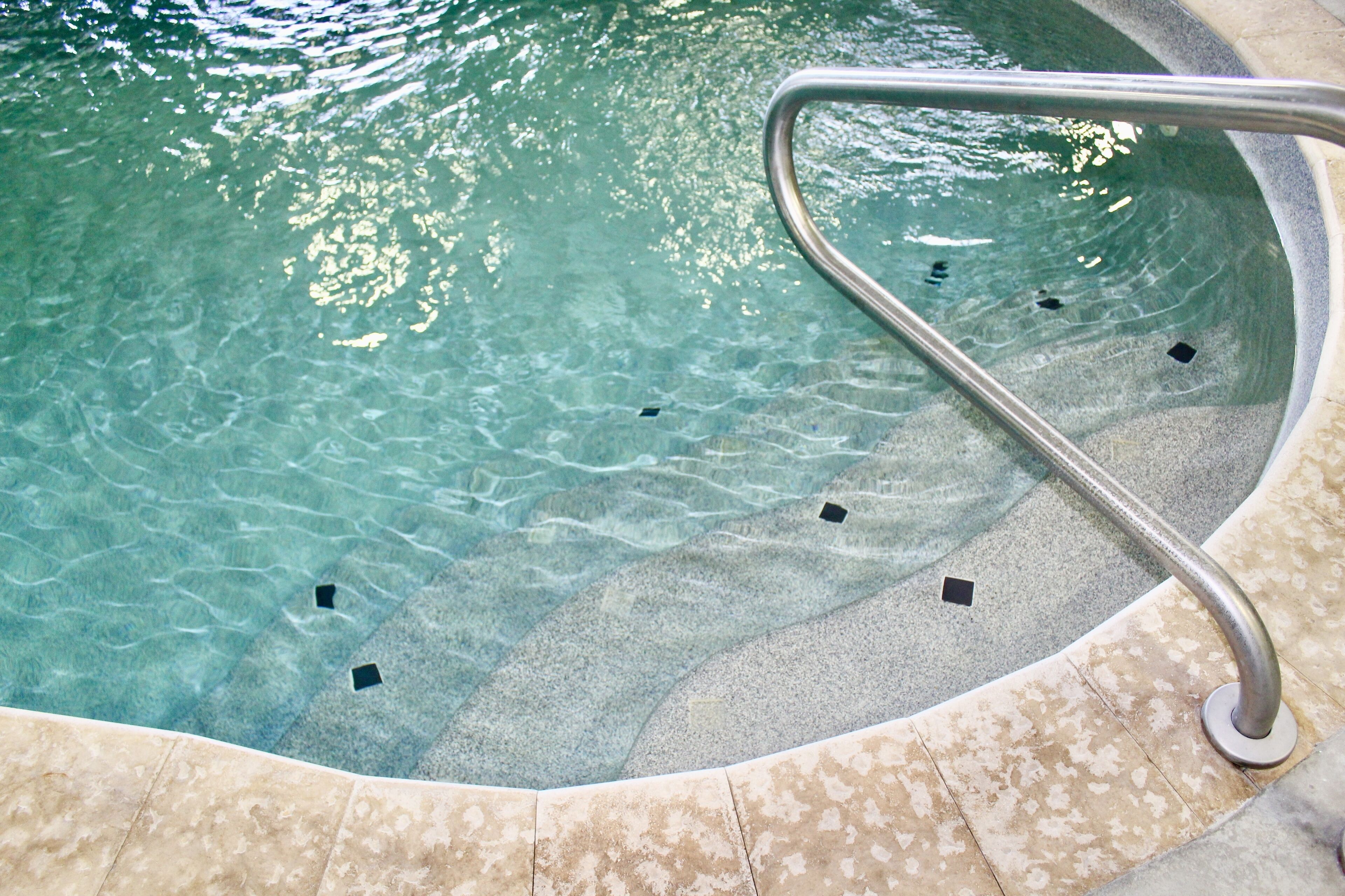 Une piscine intérieure à eau claire, dotée d’une rambarde métallique et de carreaux de pierre.