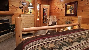 A wooden cabin bedroom with a bed, dresser, and a fireplace.