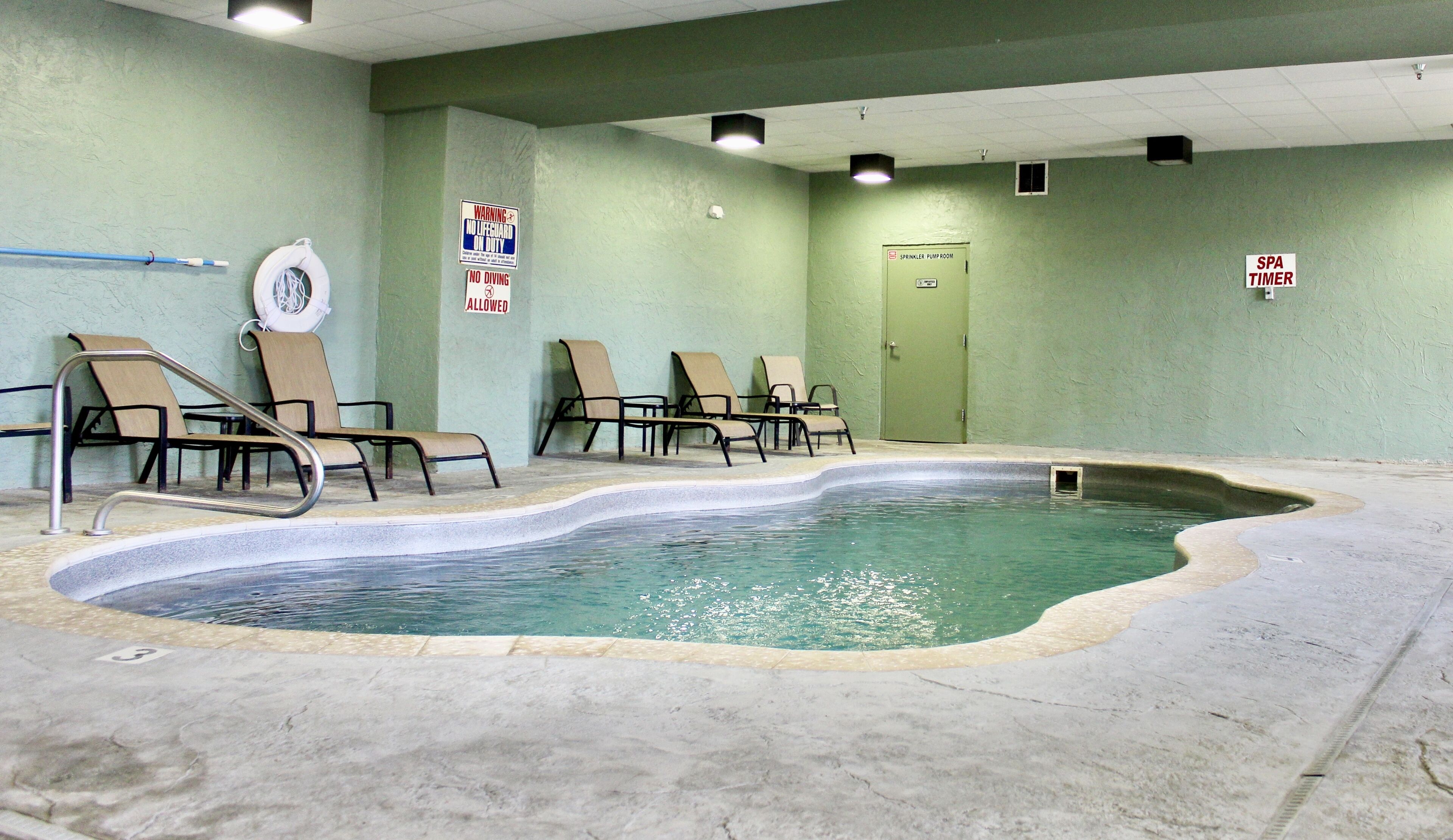 Una piscina interior con sillas de descanso, una silla de socorrista y señales que indican que no se permite bucear.