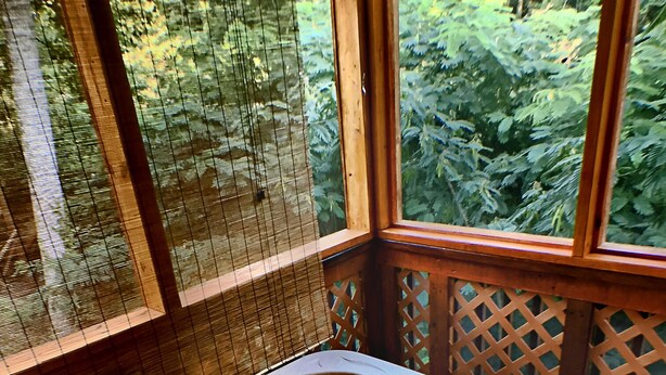 A hot tub with a view of a forest through a wooden lattice window.