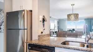 A modern kitchen with a stainless steel refrigerator, granite countertops, and a built-in dishwasher. - 🌅 Islander #307 – Sunrise Coffee & Front-Row Beach Action! 🌊🏄‍♂️ (Destin)