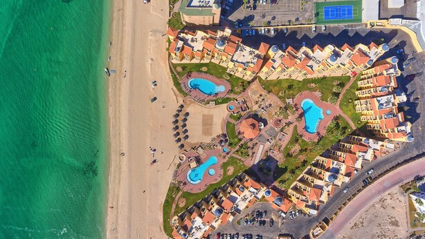 Vista aérea de un resort con múltiples piscinas, una playa y un estacionamiento.