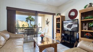 Una sala de estar con un sofá, una mesa de centro de vidrio, un televisor y una estantería.