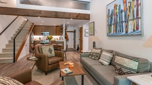 A spacious living area with a high ceiling, a staircase, a kitchen, and a dining area.