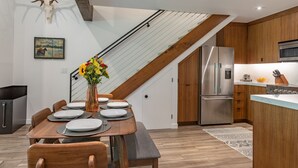 A modern kitchen with a stainless steel refrigerator, wooden cabinets, and a dining area with a wooden table set for six.