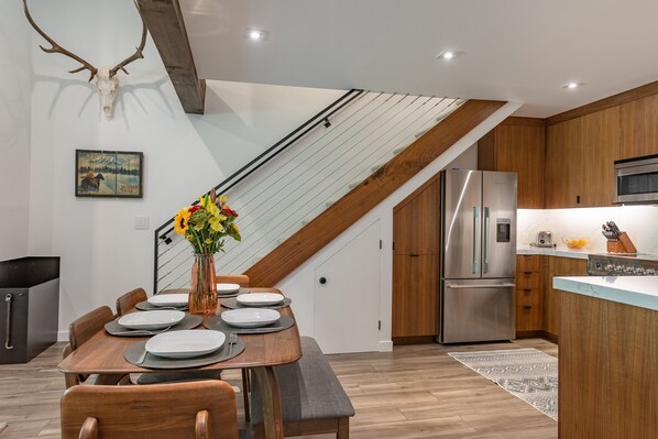 A modern kitchen with a stainless steel refrigerator, wooden cabinets, and a dining area with a wooden table set for six.