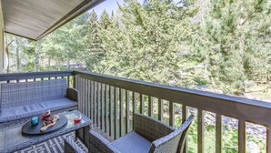A covered balcony with wicker furniture, a glass table, and a view of a forest.
