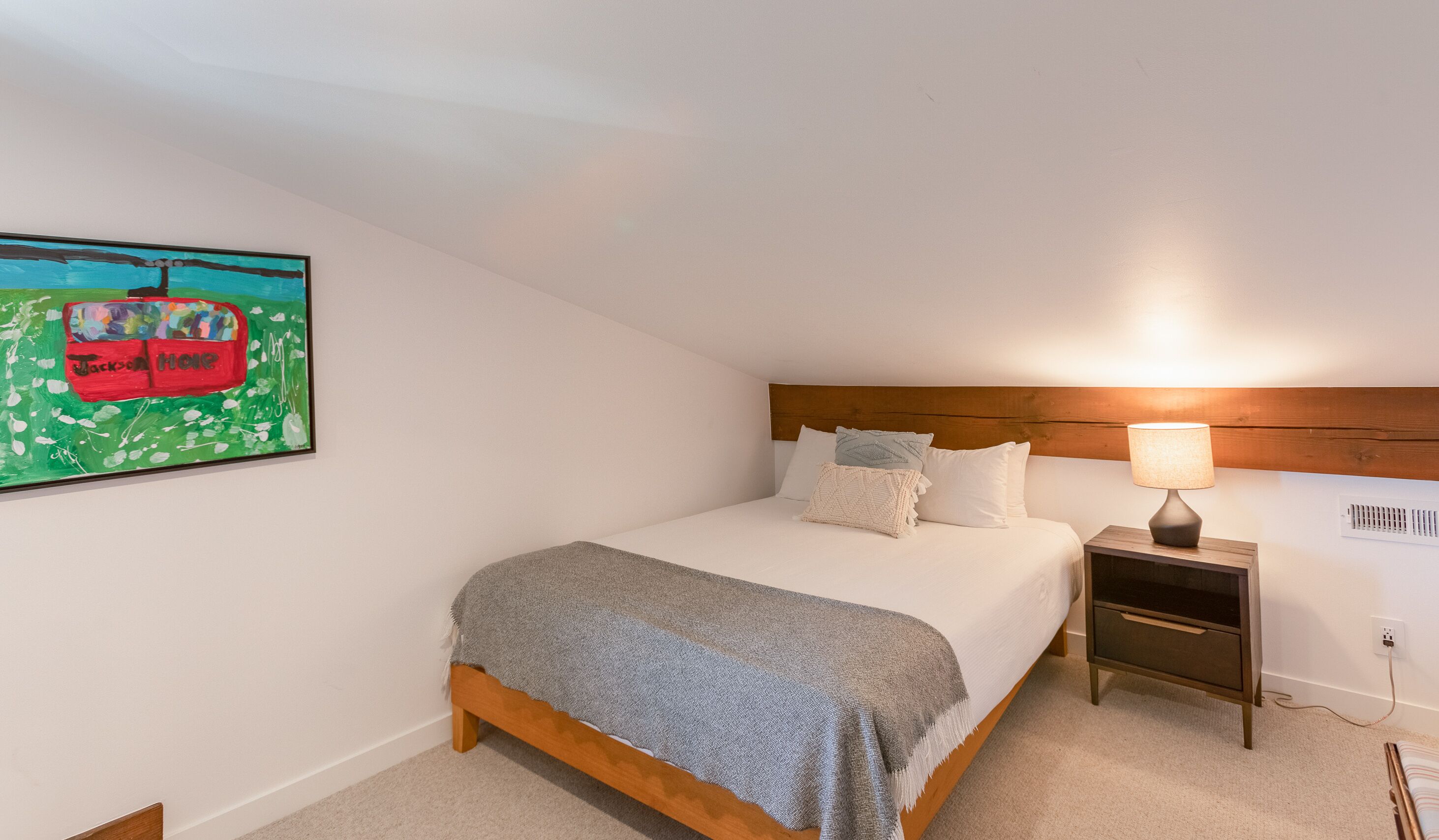 A bedroom with a bed, a nightstand, a lamp, and a painting on the wall.