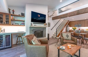 A modern living space with a fireplace, a kitchen, and a staircase.