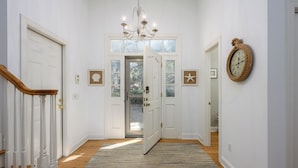 A hallway with a chandelier, a wooden staircase, and a rug.