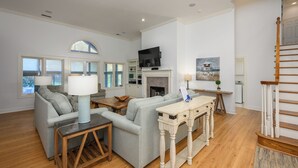 A spacious living room with a fireplace, a television mounted above it, and a staircase leading to another level.