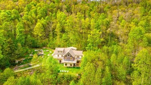 A large house surrounded by dense forest, with a well-maintained lawn and outdoor seating area. - Stoneledge Manor - Creek with Pond - Mountain Views - Pool Table (Banner Elk)