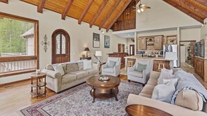 A spacious living room with a high wooden ceiling, a large window, and a kitchen area with wooden cabinets. - Stoneledge Manor - Creek with Pond - Mountain Views - Pool Table (Banner Elk)