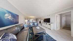 Ein modernes Wohnzimmer mit Ledersofa, Couchtisch und einem großen Gemälde einer Quallen. Im Hintergrund sind ein Fernseher und eine Küchenzeile zu sehen.