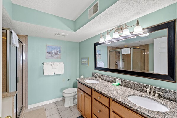 A bathroom with a large mirror, two sinks, a toilet, and a shower area.