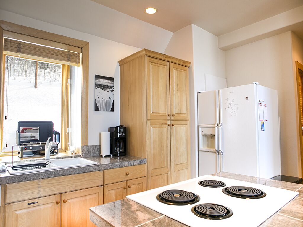 A modern kitchen with wooden cabinets, a white refrigerator, a stove, and a window with blinds.