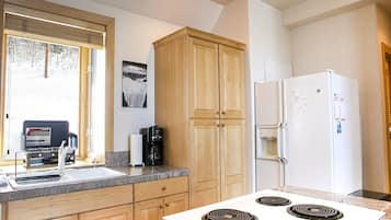 A modern kitchen with wooden cabinets, a white refrigerator, a stove, and a window with blinds.