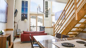Ein modernes Interieur mit Essbereich, rotem Sofa, Holztreppe und Blick ins Freie.