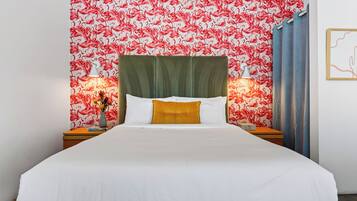 Habitación de hotel con cama, dos mesitas de noche, un cabecero tapizado en verde y una pared con estampado de flamenco rojo y blanco.