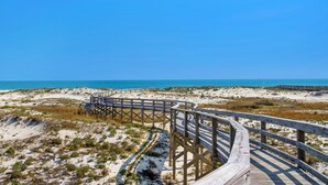 Une promenade en bois qui mène à une plage, avec un ciel bleu dégagé.